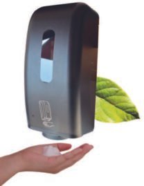 Dispensador de jabón con sensor y con una mano de bajo mientras cae el jabón. Detrás del dispensador se ve una hoja de flor.